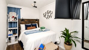 Ein Schlafzimmer mit einem Bett, einem Regal mit Dekoration, einer Topfpflanze und einem Fenster mit Jalousie.