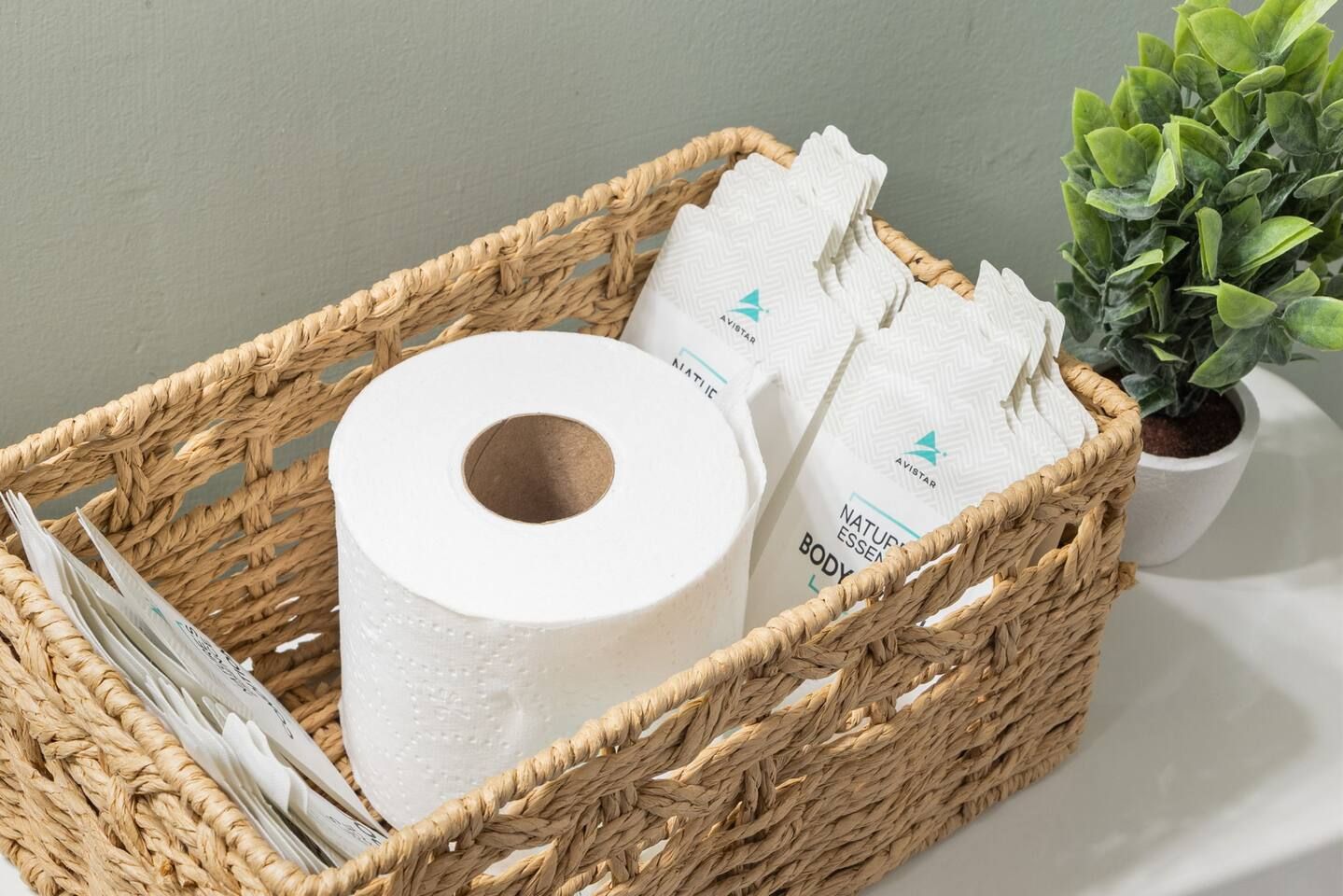 A woven basket containing a roll of toilet paper and two branded body care products.