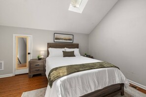 Ein Schlafzimmer mit einem Bett, Nachttischen, einem Spiegel, einem Bild an der Wand und einem Dachfenster.