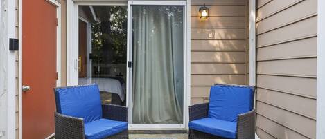 A patio with two wicker chairs and a small table, a sliding glass door, and a wall-mounted light fixture.