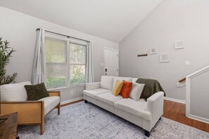 Ein Wohnzimmer mit einem weißen Sofa, einem Korbstuhl und einem gemusterten Teppich.