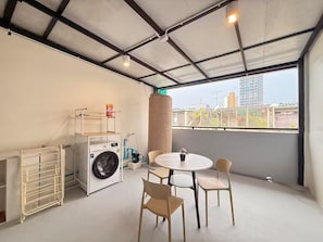 A room with a washing machine, a drying rack, a table with chairs, and a view of a cityscape through a large window. - Private Villa for 10 in Bangkok (Thanon Petchaburi, Ratchathewi)