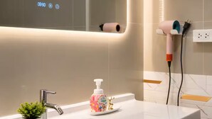 Een badkamer met een witte wastafel, een kleine potplant, een zeepdispenser en een haardroger aangesloten op een stopcontact.