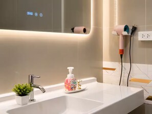 A bathroom with a white sink, a small potted plant, a soap dispenser, and a hairdryer plugged into a wall socket. - Entire home in Ratchathewi, Thailand (Thanon Petchaburi, Ratchathewi)