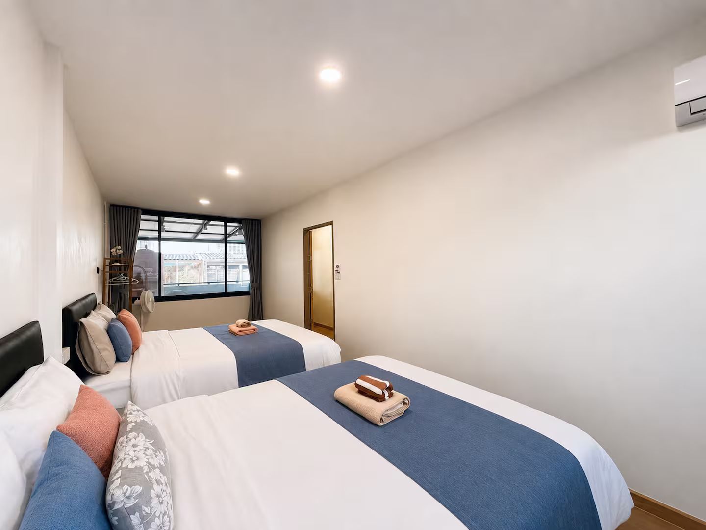 Ein Hotelzimmer mit zwei Betten, einem Fenster mit Blick, einer Tür und einer Klimaanlage.