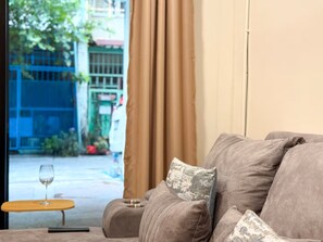 A living room with a sofa, a small table with a glass, and a view of a street outside. - Private Villa for 10 in Bangkok (Thanon Petchaburi, Ratchathewi)