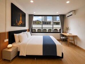 A hotel room with a bed, bedside table, desk, chair, and a large window with a view of buildings. - Entire home in Ratchathewi, Thailand (Thanon Petchaburi, Ratchathewi)