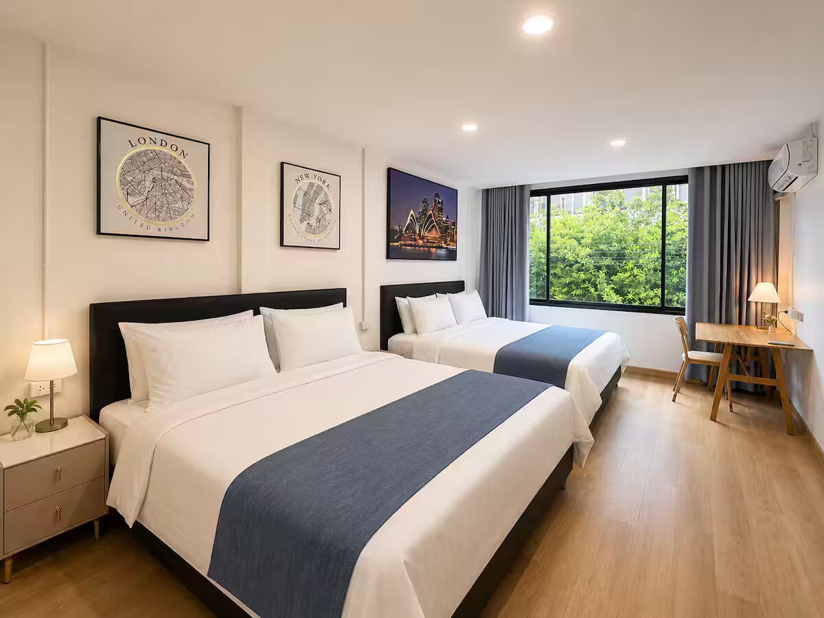 Ein Hotelzimmer mit zwei Betten, einem Schreibtisch und einem Fenster mit Blick auf Grünflächen.