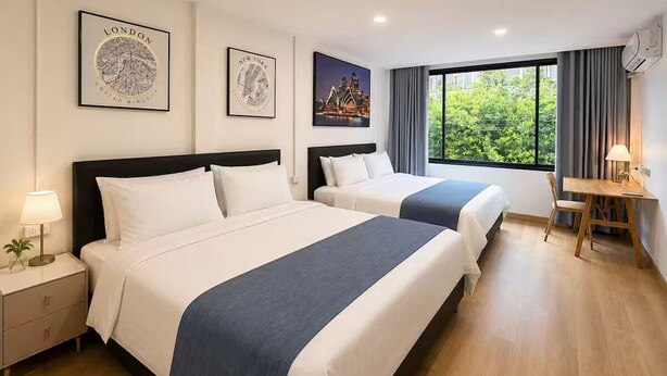 Een hotelkamer met twee bedden, een bureau en een raam met uitzicht op groen.