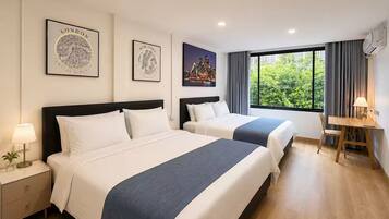 A hotel room with two beds, a desk, and a window with a view of greenery.