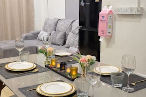 A dining table set with gold-rimmed plates, clear glasses, and candles, with a grey sofa and a refrigerator in the background. - Private Villa for 10 in Bangkok (Thanon Petchaburi, Ratchathewi)
