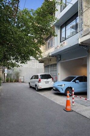 A street with two parked cars, a tree, and a building with a balcony. - Private Villa for 10 in Bangkok (Thanon Petchaburi, Ratchathewi)
