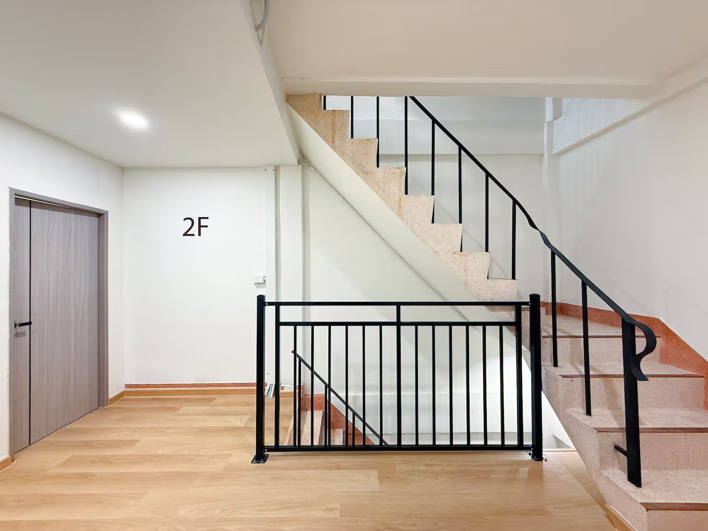 Eine Treppe mit schwarzem Metallgeländer, Holzboden und einer Wand mit einer Tür, auf der '2F' steht.