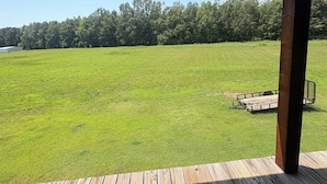 A covered wooden deck with a view of a green field and trees.