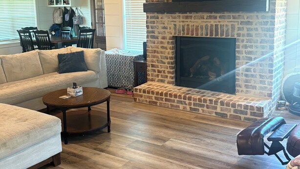 A living room with a fireplace, wooden flooring, and a ceiling fan.