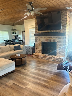 A living room with a fireplace, wooden flooring, and a ceiling fan.