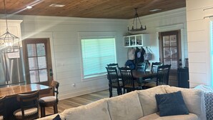 A spacious living room with a wooden ceiling, a large beige sofa, and a dining area with a wooden table and chairs.