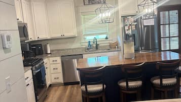 A kitchen with white cabinets, a stainless steel refrigerator, a wooden ceiling, and a bar area with stools.