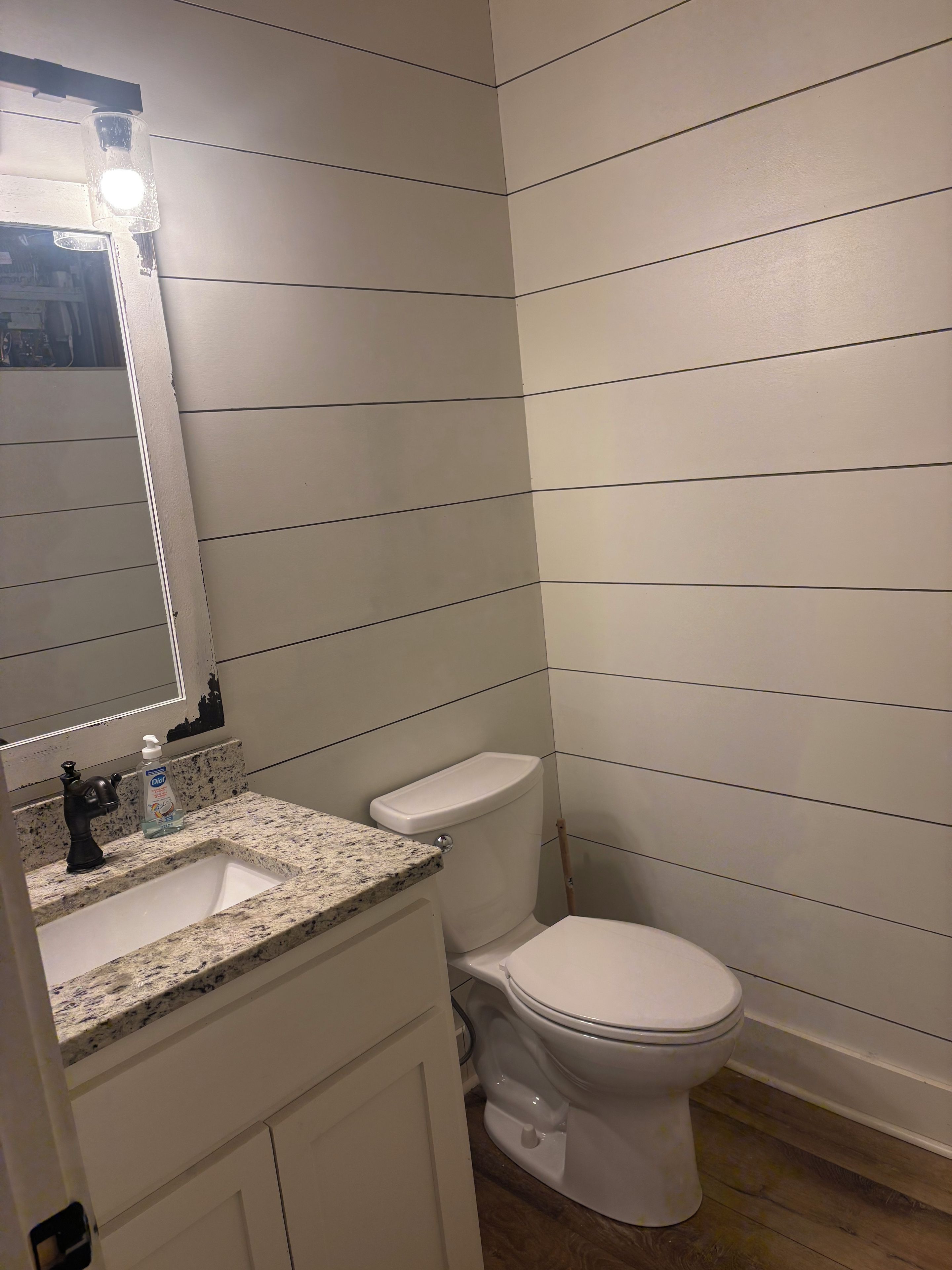 Un baño con inodoro blanco, lavamanos con dispensador de jabón y espejo con luces.
