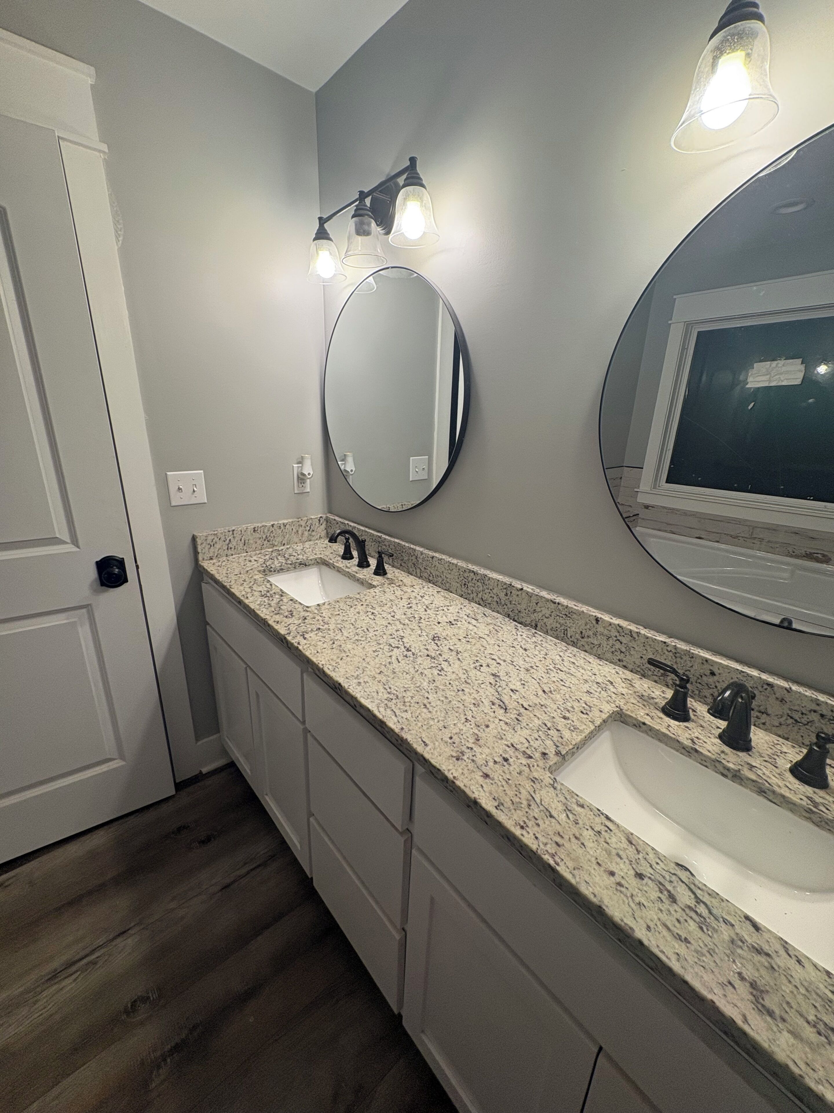 A bathroom with a double sink, a mirror, and a light fixture above the mirror.