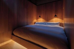 Une chambre avec un mur revêtu de panneaux en bois, un lit avec une literie blanche et deux lampes suspendues.