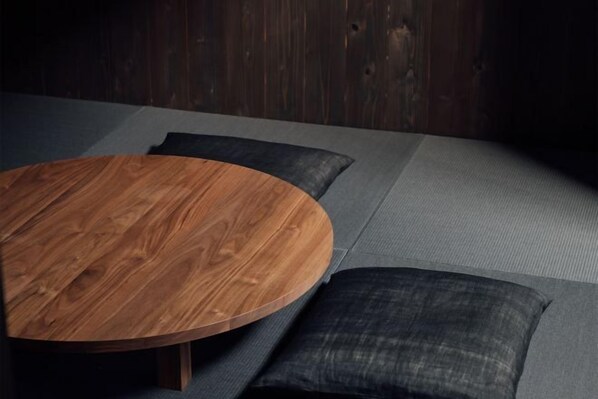 Une table ronde en bois, accompagnée d’un canapé gris et de coussins foncés.