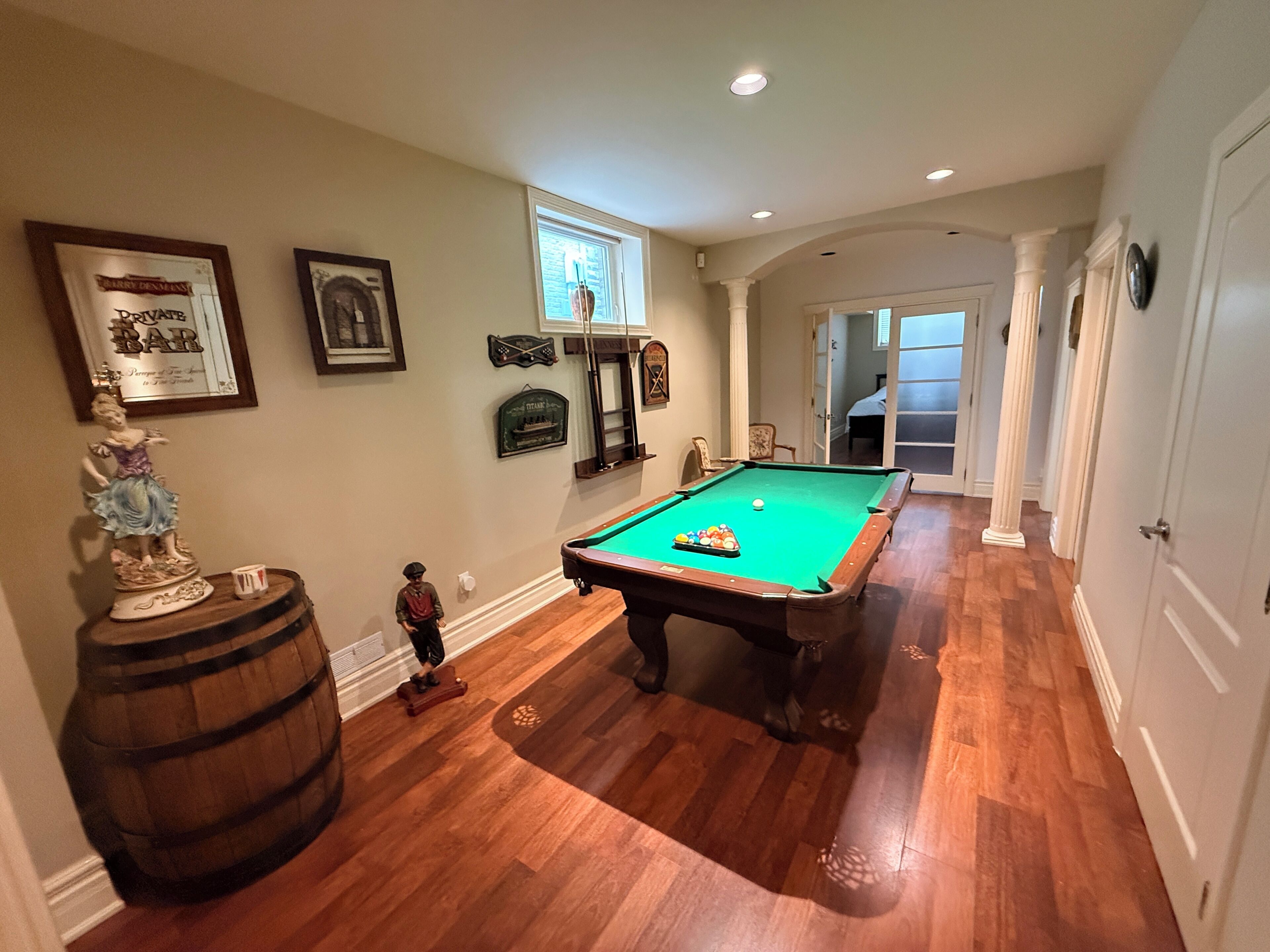 A pool table in a room with wooden flooring, a bar area, and a billiards cue rack.
