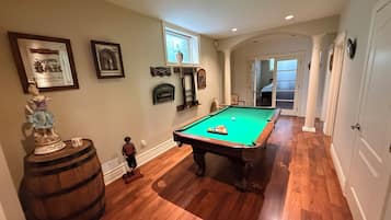 A pool table in a room with wooden flooring, a bar area, and a billiards cue rack.