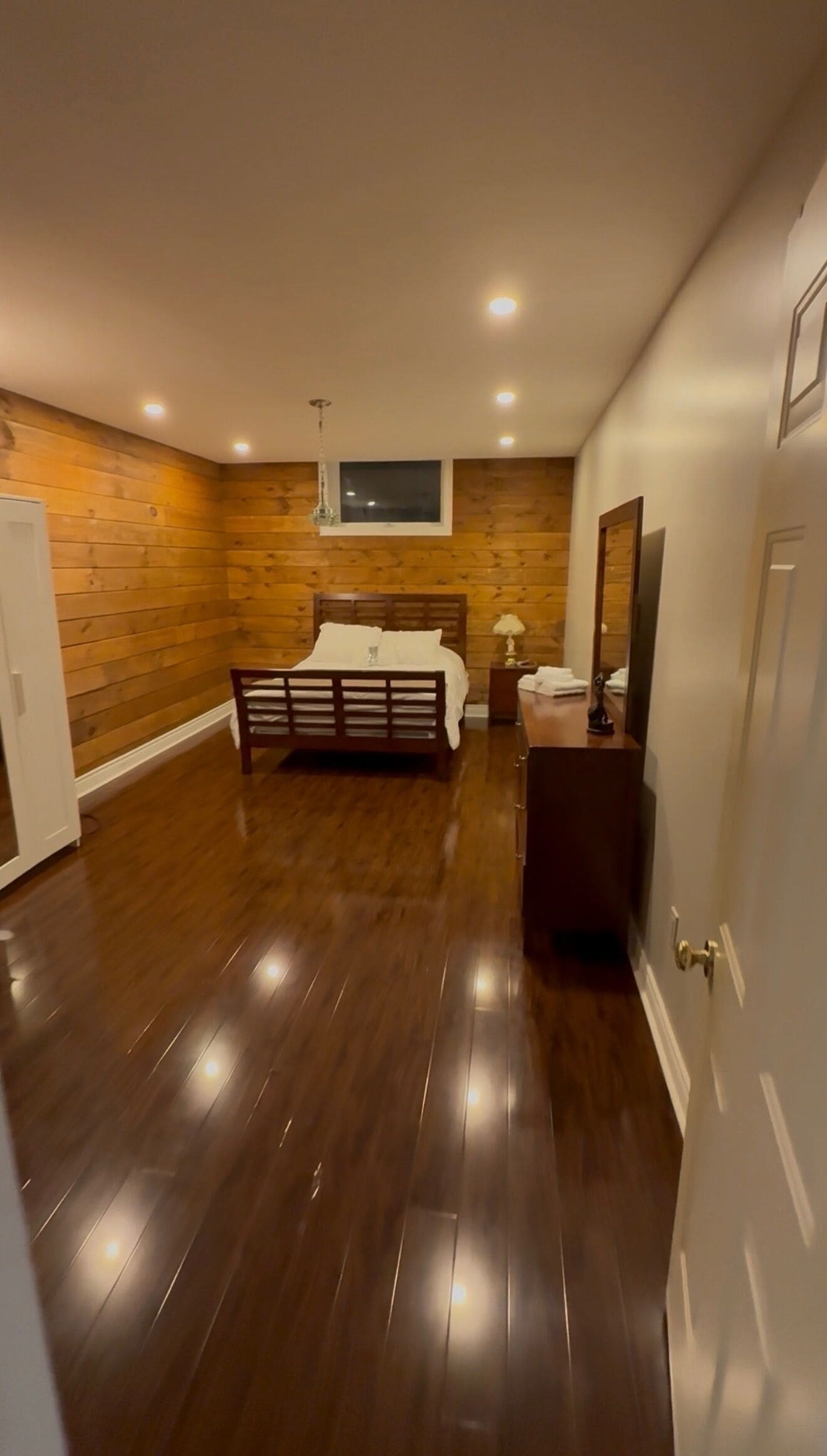 A bedroom with a wooden floor, a bed, a nightstand, and a mirror.