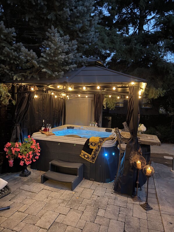A hot tub with a canopy, surrounded by stone tiles, and a flower arrangement.