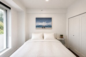 Ein Schlafzimmer mit einem Bett, einem Fenster, einem Strandbild und einem Kleiderschrank.