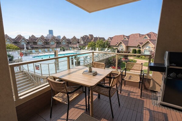 Un balcón con vista a la piscina, mobiliario exterior y una parrilla.
