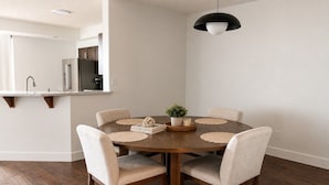 A dining area with a round wooden table, six chairs, a potted plant, and a book titled 'The Beauty of Imperfection'. - 3 bedroom downtown condo - sleeps 6 - lake & pools (Kelowna)