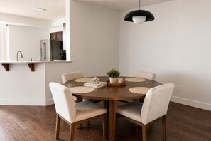 Un comedor con una mesa redonda de madera, seis sillas, una planta en maceta y un libro titulado 'The Beauty of Imperfection'.