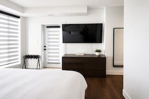 A bedroom with a bed, a dresser, a television mounted on the wall, and a door with blinds. - 3 bedroom downtown condo - sleeps 6 (Kelowna)