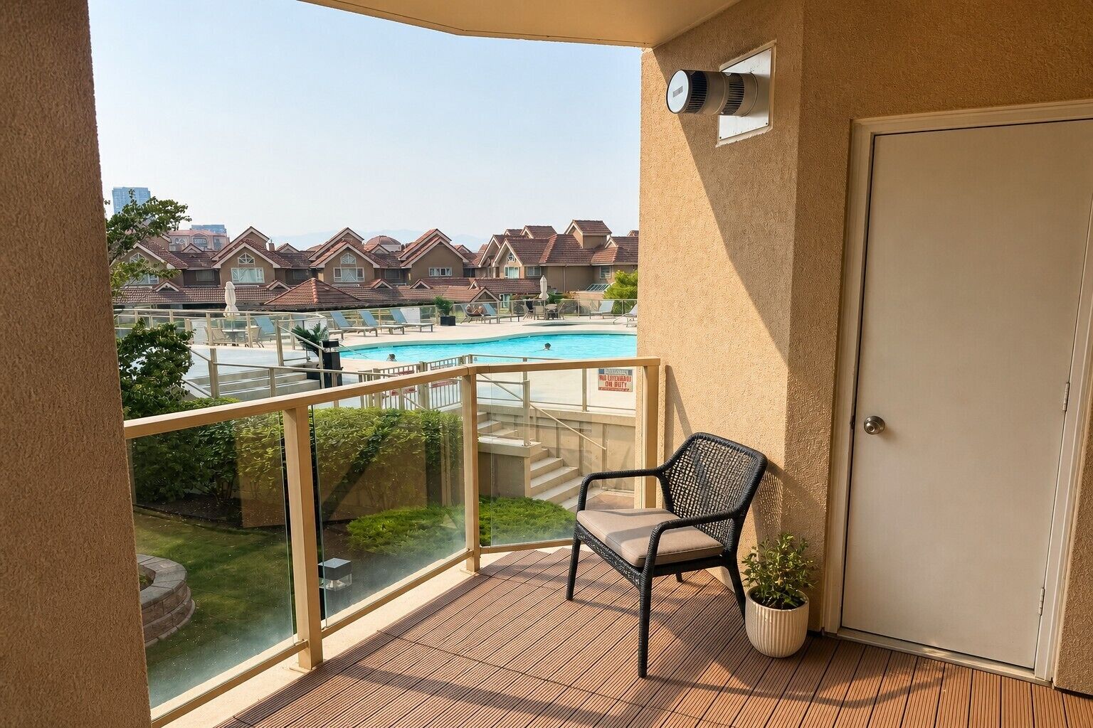 A balcony with a view of a swimming pool, a chair, a potted plant, and a door.