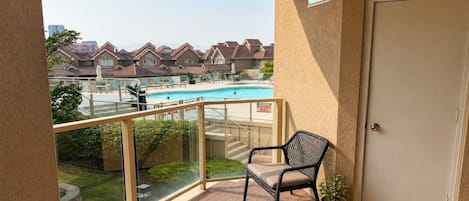 A balcony with a view of a swimming pool, a chair, a potted plant, and a door.