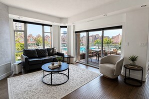 Una sala de estar moderna con sofá, mesa de centro y vista a una piscina y edificios.