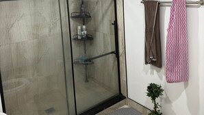 Et moderne badeværelse med en glasvæg omkring brusenichen, toilet, håndvask og et håndklædestativ med et mønstret håndklæde.