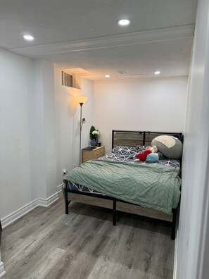 A bedroom with a bed, bedside lamp, and a small table with a plant. - 3-bedroom basement unit in Vaughan nice stay close to plazas outlets furnished (Vaughan)