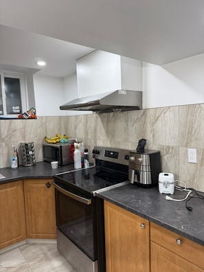 A modern kitchen with a stainless steel stove, oven, and a range hood. There is a microwave, a coffee maker, and a Starfrit toaster on the counter. - 3-bedroom basement unit in Vaughan nice stay close to plazas outlets furnished (Vaughan)