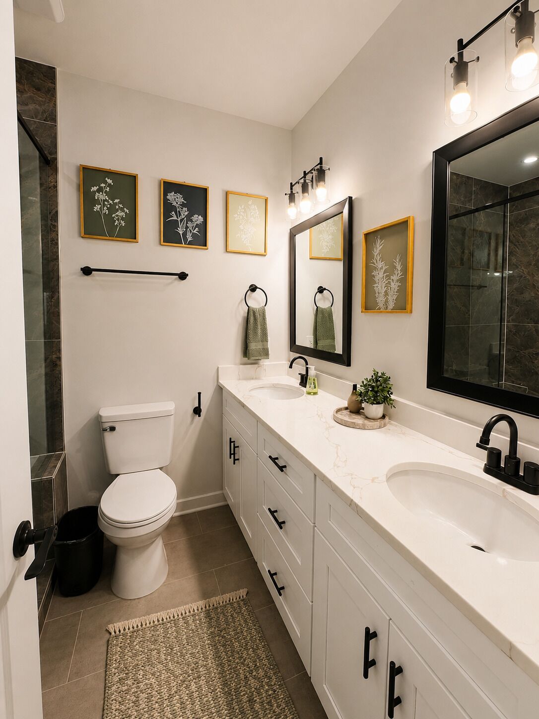Un baño moderno con inodoro, lavamanos y espejo. Hay fotografías enmarcadas en la pared y una pequeña planta en la encimera.