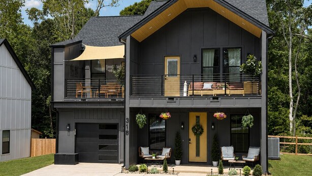 Ein zweistöckiges Haus mit Garage, Balkon und einer Veranda mit Sitzgelegenheit.