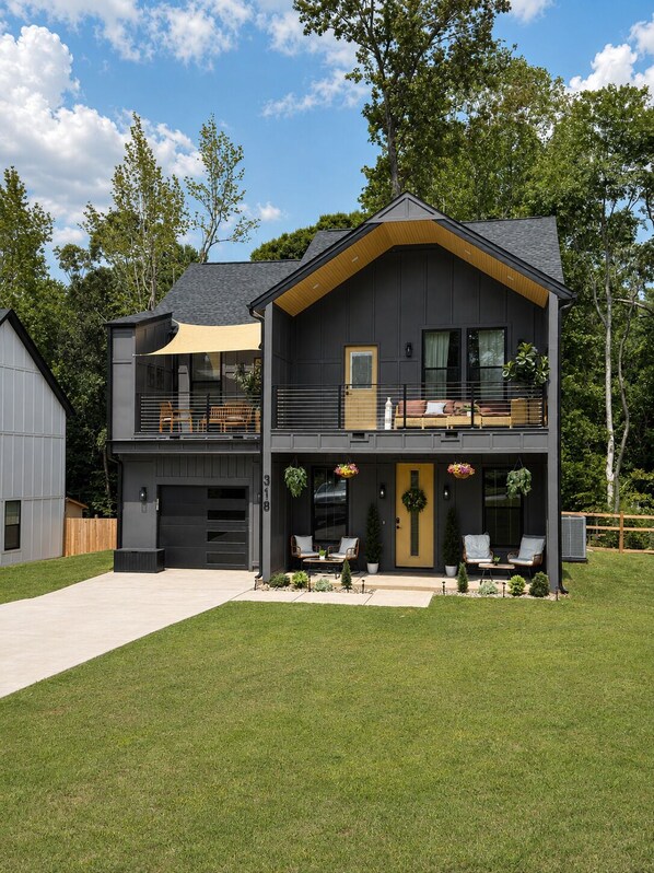 A two-story house with a garage, a balcony, and a front porch with seating.