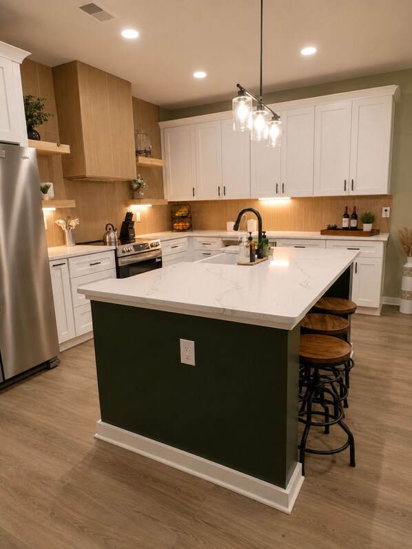 Una cocina moderna con una isla central, muebles de cocina blancos y un refrigerador de acero inoxidable.