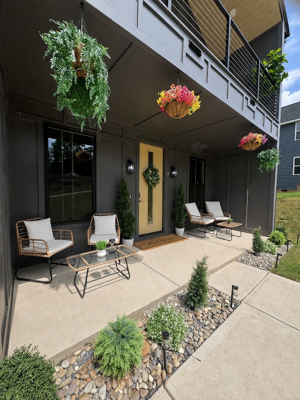 Et moderne hus med en overdækket terrasse, udendørs møbler og blomsterkasser.