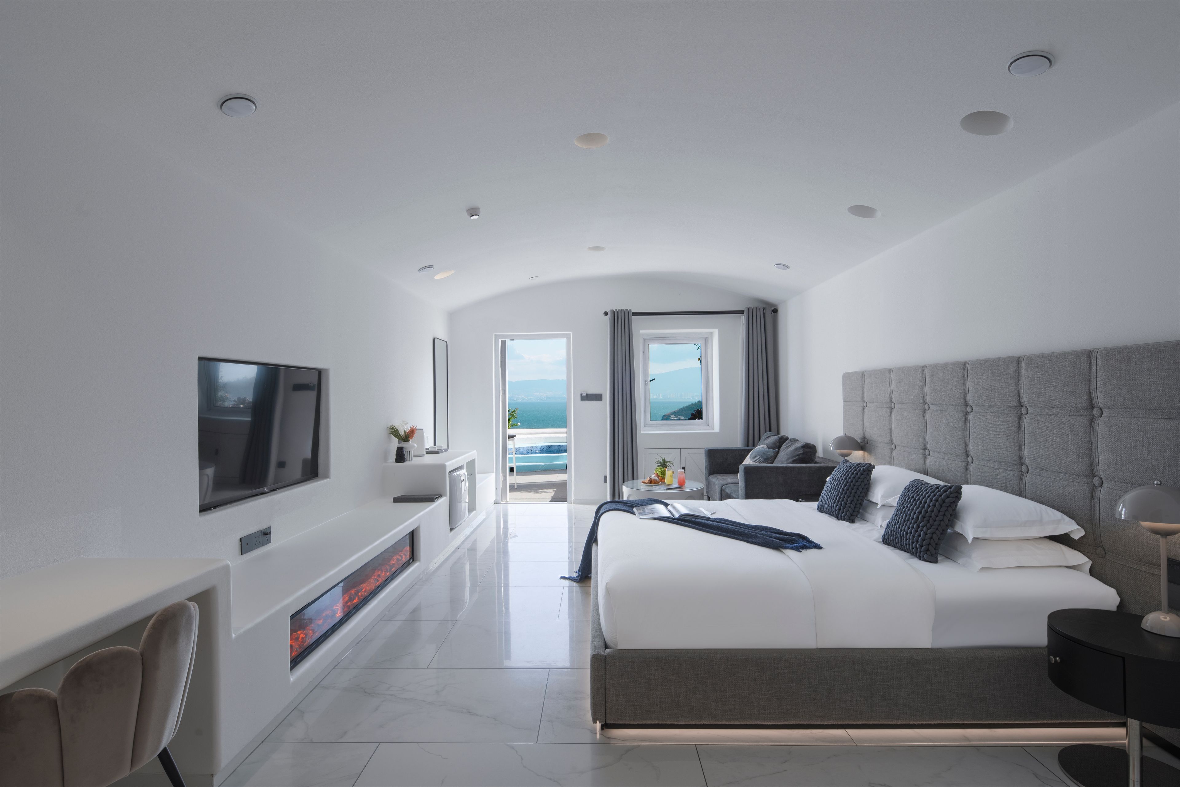 Habitación de hotel moderna con una cama grande, televisión, chimenea y vista al mar.