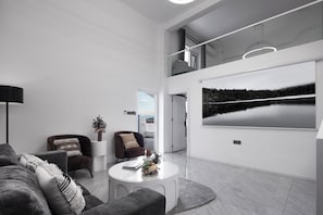 Een moderne woonkamer met een bank, fauteuils, een salontafel en een groot raam met uitzicht op een meer.