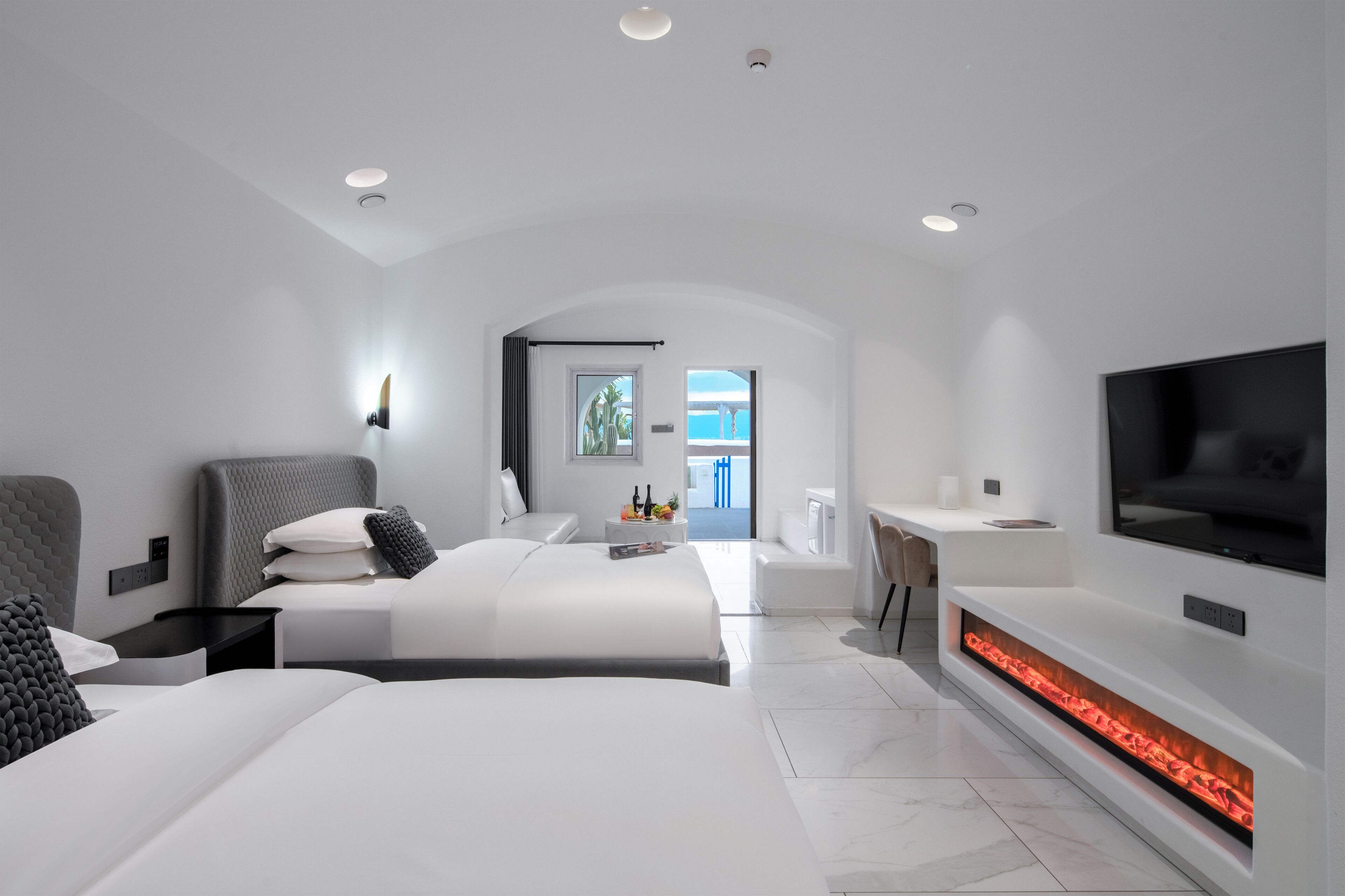 A modern hotel room with a large bed, a TV, a fireplace, and a view of the outdoors.