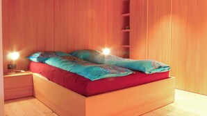 A modern bedroom with a wooden bed, red bedding, and a nightstand with a lamp. - Nice apartment for 4 people with WIFI, TV and balcony (Zermatt)